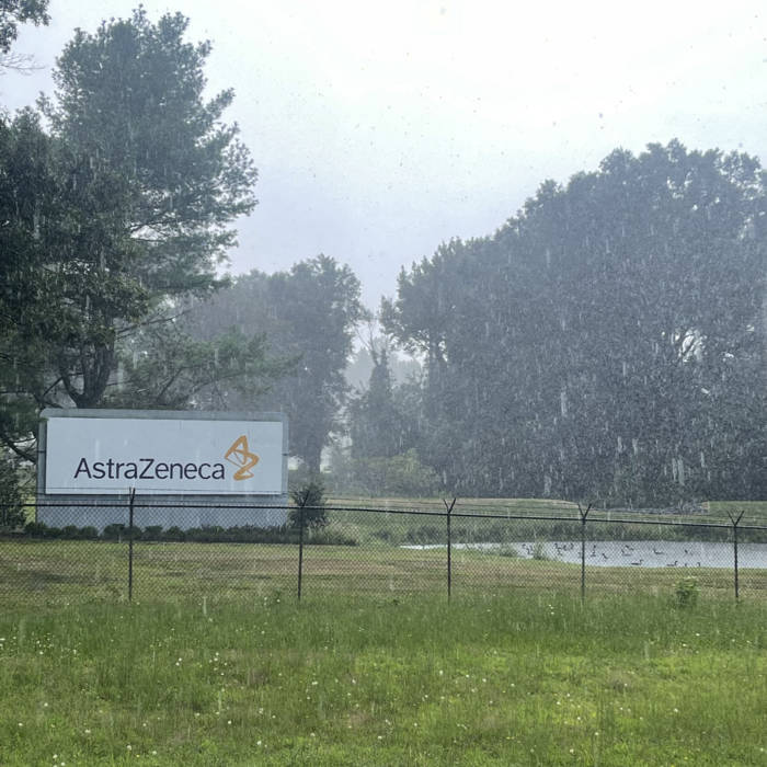 A photograph of grass and a pond with geese hanging out, alongside a large sign reading “AstraZeneca”